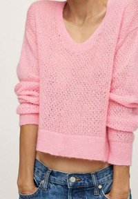 Pull court rose en maille avec une maille lâche et ouverte, doté de manches longues et d'un large décolleté en V. Texture douce avec des poignets côtelés.
