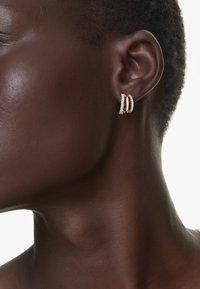 Pendientes de aro en oro rosa con pequeñas piedras transparentes. Diseño de doble aro con un acabado pulido, que destaca una estética elegante y moderna.