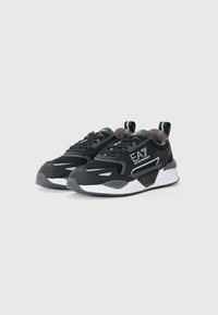 Zwarte sport sneakers met een textiel bovenwerk, witte accenten, een gevoerde kraag en een dikke rubberen zool met een kenmerkend profiel.