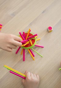 Gioco impilabile colorato con bastoncini di plastica rosa, gialli e verdi disposti attorno a una base circolare con motivo di anguria su una superficie di legno.