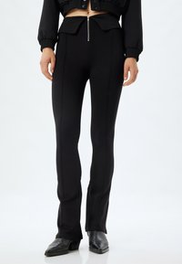 Pantalons ajustés noirs avec taille haute, fermeture éclair et détails de couture. Texture lisse avec un léger évasement en bas.
