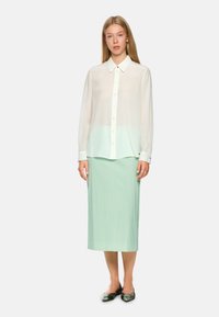 White, sheer long-sleeve blouse with a button-down collar, paired with a mint green pleated midi skirt. Flat shoes feature a patterned design.