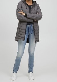 Grå vadderad rock med huva, med horisontell quiltad struktur. Matchas med ljusblå smala jeans och vita sneakers.