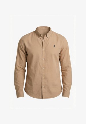 Camisa beige de manga larga con botones, cuello abotonado y pequeño emblema de árbol negro en el pecho izquierdo.
