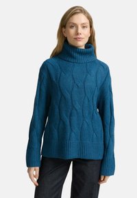 Pull en tricot turquoise à col roulé haut, présentant un ourlet côtelé et des manches longues. Texture douce et motif ondulé prononcé.