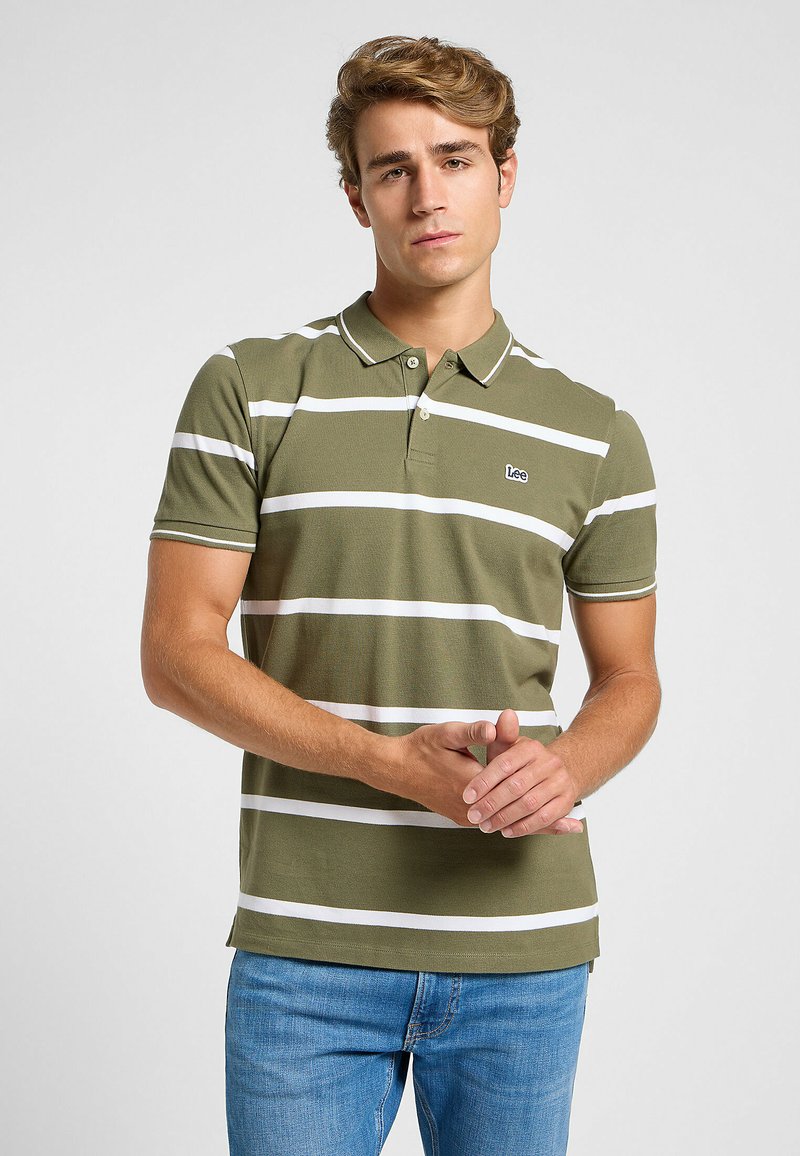 Polo verde oliva con rayas horizontales blancas, mangas cortas y cuello. Pequeño logo en el pecho izquierdo. Material de algodón. Corte casual.