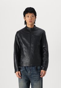 Giubbotto in pelle nera con colletto alto, chiusura frontale con zip e una tasca con zip sul petto. Presenta una texture liscia e una vestibilità su misura.