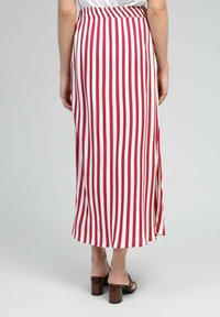 Jupe longue et fluide avec des rayures verticales rouges et blanches, taille élastique, fente sur le côté et ourlet tombant sous les chevilles. Texture de tissu douce.