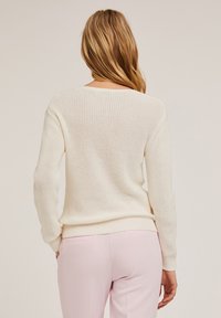 Crème-kleurige gebreide trui met een ontspannen pasvorm en lange mouwen, voorzien van een geribde zoom en een textuurpatroon. Draag het met lichtroze broek.