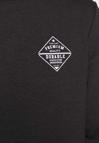 Černá mikina s bílým logem ve tvaru diamantu a textem: "Pier One Premium Quality Durable Authentic Clothing Since 2011."
