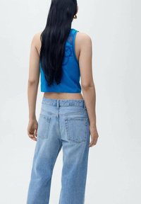 Plavi bezriječni crop top s teksturiranim uzorkom, uparen s svijetloplavim ležernim trapericama koje imaju dva stražnja džepa.