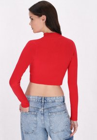 Top corto rosso a costine con maniche lunghe e collo alto, abbinato a jeans a vita alta blu chiaro, dotati di tasche posteriori.