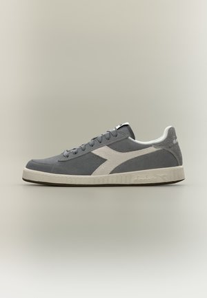 Grå ruskind lav-top sneaker med hvid sidestribe, hvid sål og snørebånd, vist fra ydersiden på en lys baggrund.