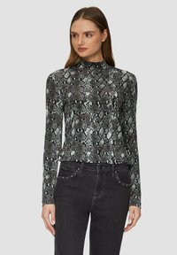 Haut à manches longues dans un motif imprimé serpent noir et gris, avec un col montant et un tissu doux et extensible. Associé à un jean noir ajusté.