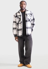 Camicia di flanella a scacchi in bianco e nero con due tasche sul petto, jeans grigi e calzature beige. Tessuto piatto e morbido con vestibilità rilassata.