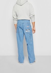 Vaaleansiniset farkku cargo-housut, joissa on rento leikkaus, useita taskuja, logo-patch ja kulunut tekstuuri.