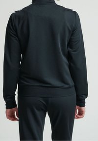 Black athletic jacket with a smooth texture, high collar, and contrasting shoulder accents. Fitted design, paired with matching bottoms.
