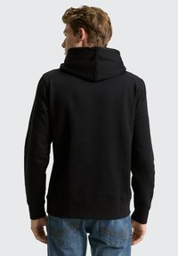 Schwarzer Hoodie mit doppellagiger Kapuze, gerippten Bündchen und glatter Textur, kombiniert mit blauen Jeans. Ansicht von hinten.