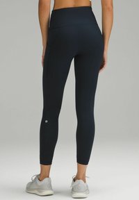 Leggings blu navy a vita alta realizzati in materiale elastico. Presentano tasche laterali e un dettaglio del logo vicino alla caviglia. Texture liscia.