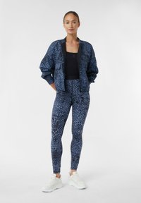 Giacca bomber con stampa leopardata blu abbinata a leggings coordinati. Tessuto morbido e elasticizzato, abbinato a sneakers bianche. Semplice top nero monocromatico sotto.