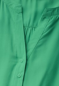 Camicetta verde con scollo a V, dettagli plissettati e chiusura con bottoni. Realizzata in tessuto morbido e leggero.