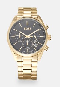 Montre en acier inoxydable doré avec un cadran noir, trois sous-cadrans, affichage de la date et graduations tachymétriques. Équipée d'un bracelet métallique à maillons.