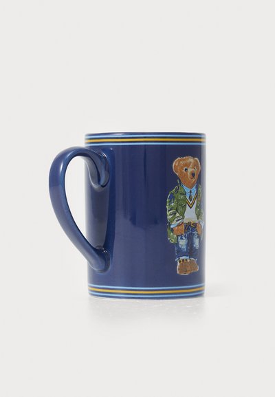 Tasse en céramique bleu marine avec un motif d'ours en tenue décontractée, détaillé avec une veste verte et un jean, souligné par des rayures jaunes et bleues.