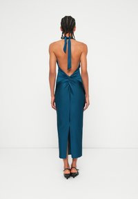 Turkizna satenasta koronkasta obleka z nizkim hrbtom, nagubanjem na pasu in sprednjim razporkom. Zavezuje se okoli vratu, elegantna silhueta in gladka tekstura.