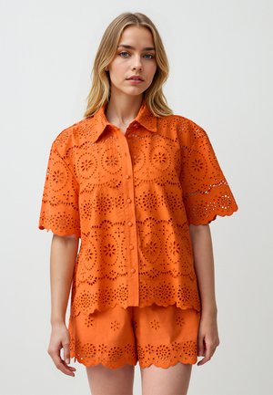 Oranje geborduurd overhemd met korte mouwen, voorzien van florale uitsparingen, knoopsluiting aan de voorkant en gegolfde randen, gecombineerd met bijpassende shorts.