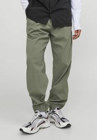 Pantalones jogger de tiro bajo en verde claro, confeccionados con material ligero y con puños elásticos. Combinados con zapatillas deportivas blancas, negras y rojas.