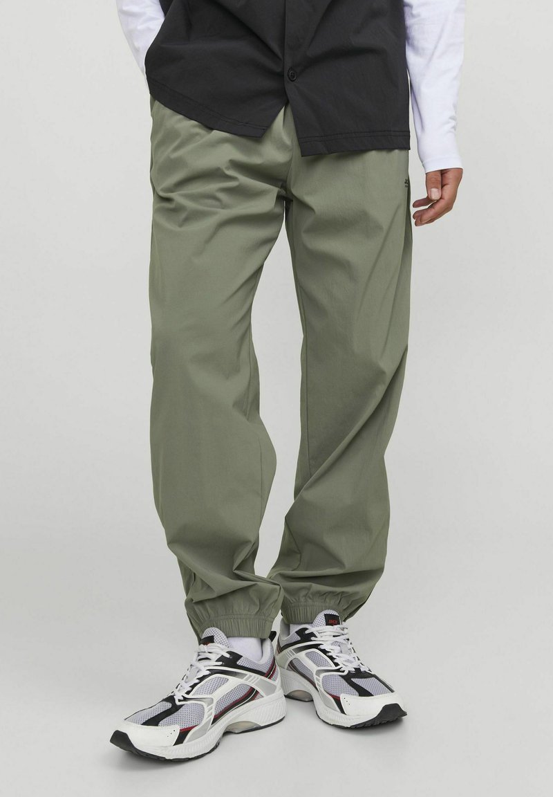 Pantalones jogger de tiro bajo en verde claro, confeccionados con material ligero y con puños elásticos. Combinados con zapatillas deportivas blancas, negras y rojas.