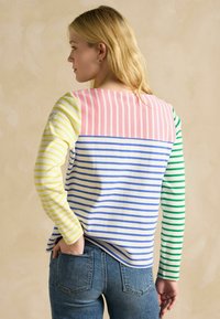 Pika, kollase, rohelise ja sinise horisontaalsete triipudega pikad varrukad särk heledal taustal. Puuvillane materjal, mugav lõige.