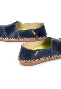 Zapatos de cuero navy tipo slip-on con ribete de fibra natural tejida y forro interior en verde lima. Incluye detalles de costura y una pequeña etiqueta de logo.