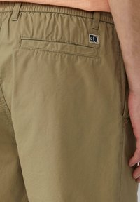 Beige Cargo-Shorts mit elastischem Bund, einer Gesäßtasche und einem kleinen Logo-Tag. Der Stoff wirkt leicht und strukturiert.