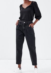Blouse noire à col en V avec manches bouffantes, associée à un jean denim taille haute à lavage foncé. Des baskets blanches accentuent le look décontracté.