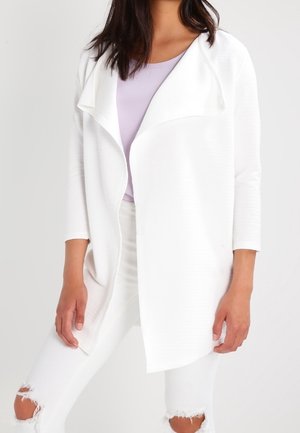 White soft-textured cardigan with an open front and draped collar, paired with a lavender top and distressed white jeans.