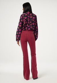 Zwart blouse met lange mouwen en een roze bloemenpatroon, gecombineerd met bordeauxrode flanelle flared broek. Bevat een klassieke shirtkraag en details aan de achterkant.