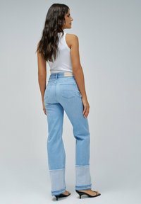 Svijetloplave traperice s visokim strukom, širokim nogavicama i rastrganym rubom. Sadrže detalje od zakrpanog materijala u svijetloj plavoj boji.