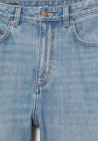 Lysblå denimjeans tæt på, der viser forlommer, bæltestropper, metal knap og syningsdetaljer på lynlåsgylp.