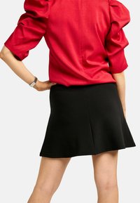 Bluza roșie cu mâneci bufante, asortată cu o fustă mini neagră evazată. Bluza are un finisaj texturat, în timp ce fusta este netedă și mulată.