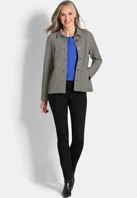 Grijze gecheckte blazer met knopen, gecombineerd met een blauwe top en zwarte slim-fit broek. Zwarte haklaarzen maken de look af.