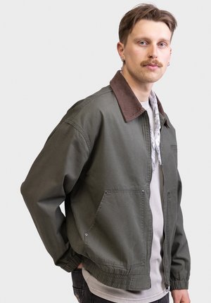 Olive green jacket with brown corduroy collar, zip closure, two front pockets, and elastic cuffs. Features a relaxed fit and lightweight material.