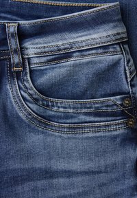 Close-up van een zak van blauwe spijkerbroek met dubbele stiknaad, een riemlus en twee metalen klinknagels aan de zijnaden.