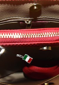 Interieur van een rode handtas met een zilveren bedel in de vorm van de Italiaanse vlag, een zwarte schouderband en een getextureerde ritsvak.