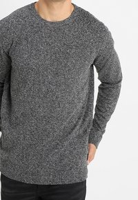 Suéter gris de punto con cuello redondo, mangas largas y un acabado texturizado. La tela parece cálida y de estilo informal.