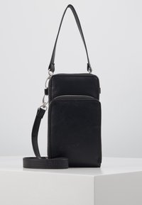 Mustasta nahasta valmistettu ristiselkkä laukku, jossa on hopeiset yksityiskohdat, kaksi vetoketjullista osiota ja säädettävä hihna. Tasainen pinta, kompakti suorakulmainen muoto.