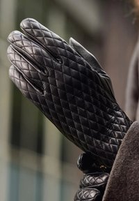 Zwarte leren handschoenen met een gewatteerd patroon, een gladde textuur en een nauwsluitend ontwerp, met naden en zonder zichtbare hardwareaccenten.
