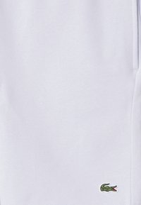 Weiße Baumwollshorts mit einem kleinen grünen Krokodil-Logo. Glatte Textur mit Seitentaschen und elastischem Bund.