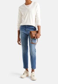 Lättviktig, creamfärgad, stickad tröja med V-ringning, blå cropped jeans, vita sneakers och en liten brun handväska med kedjeaxelrem.