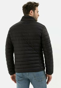 Sort puffjakke med kviltet design, høj krave og to knapper på ryggen. Bæres over lyseblå jeans.